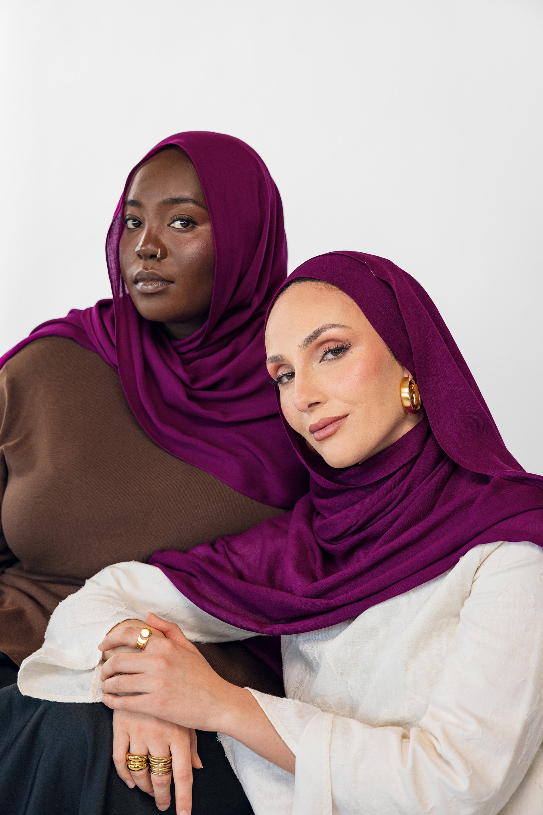 Two women wearing purple hijabs on a white background