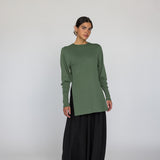 Person wearing a green long-sleeve top and black pants on a white background