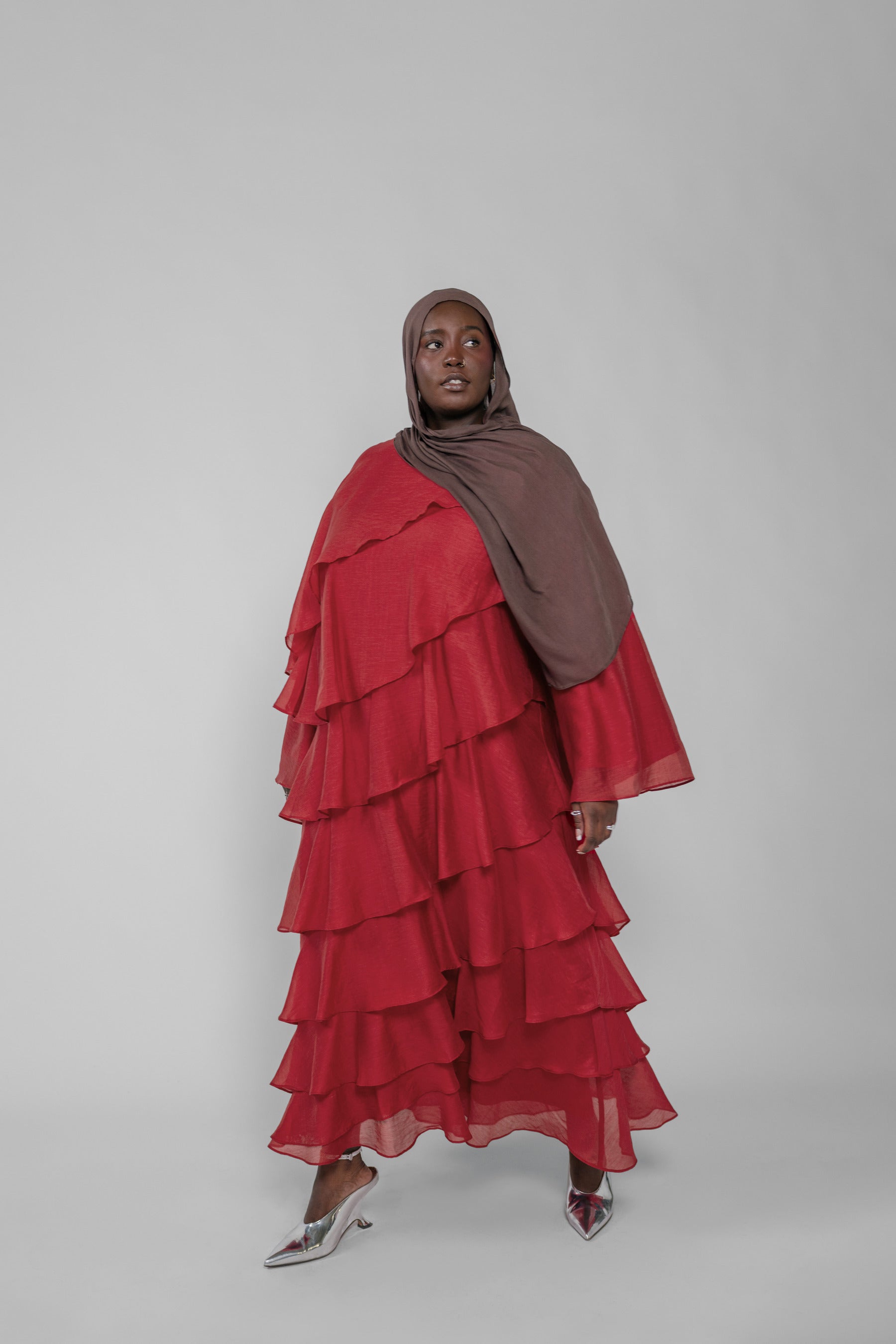 Woman wearing a red layered dress and brown hijab on a white background