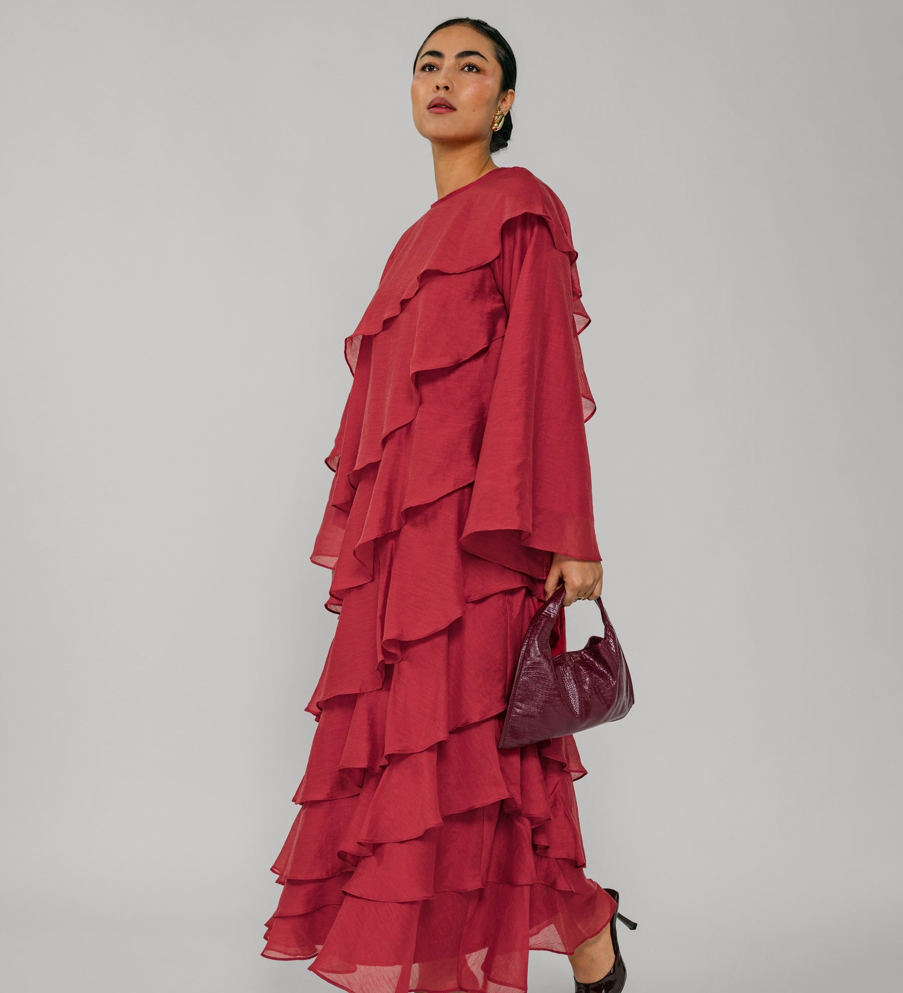 Woman wearing a red ruffled dress holding a matching handbag against a gray background