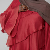 Person wearing a red layered dress and brown hijab against a plain background