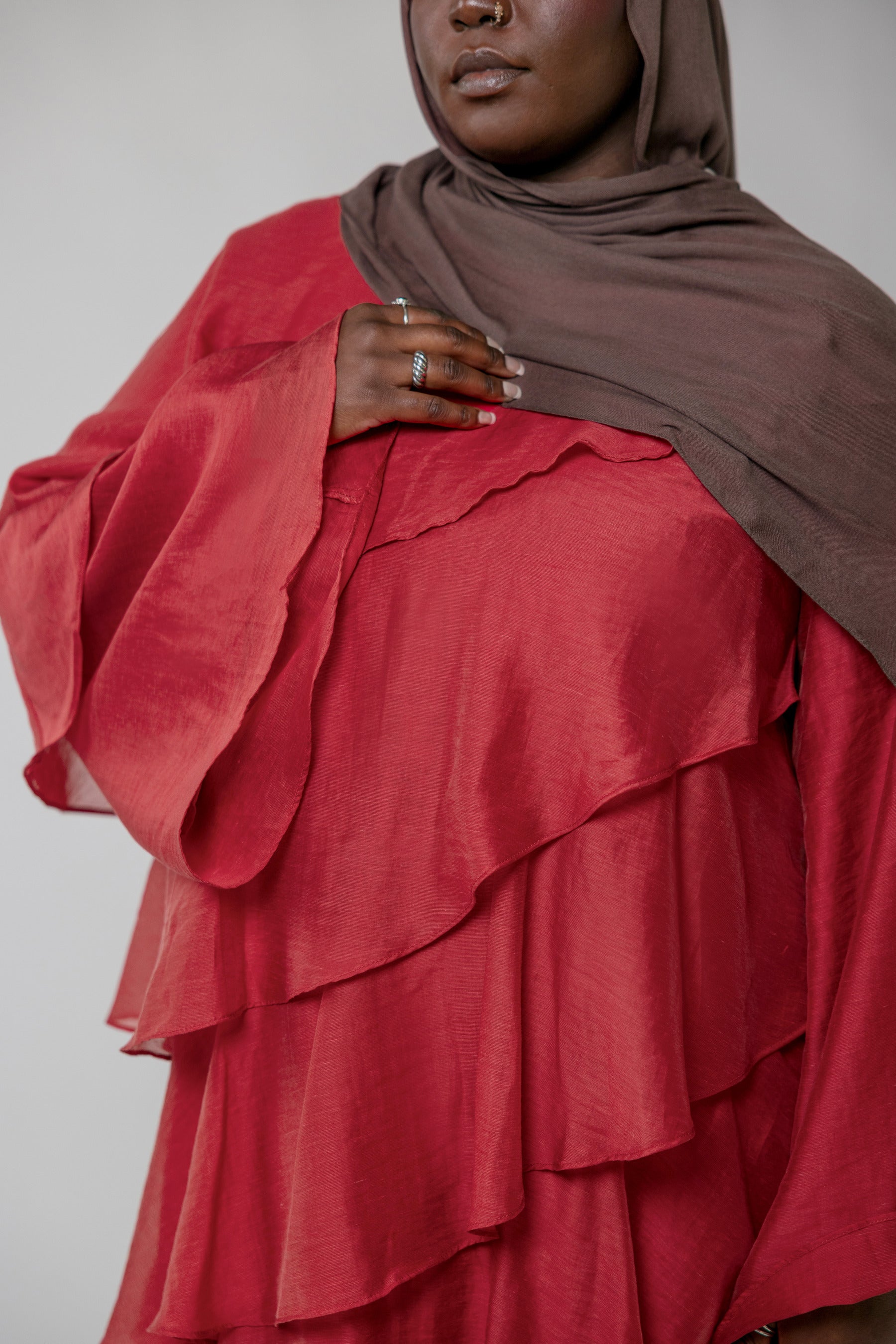 Person wearing a red layered dress and brown hijab against a plain background