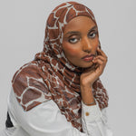 Woman wearing a giraffe patterned hijab and white shirt against a plain background