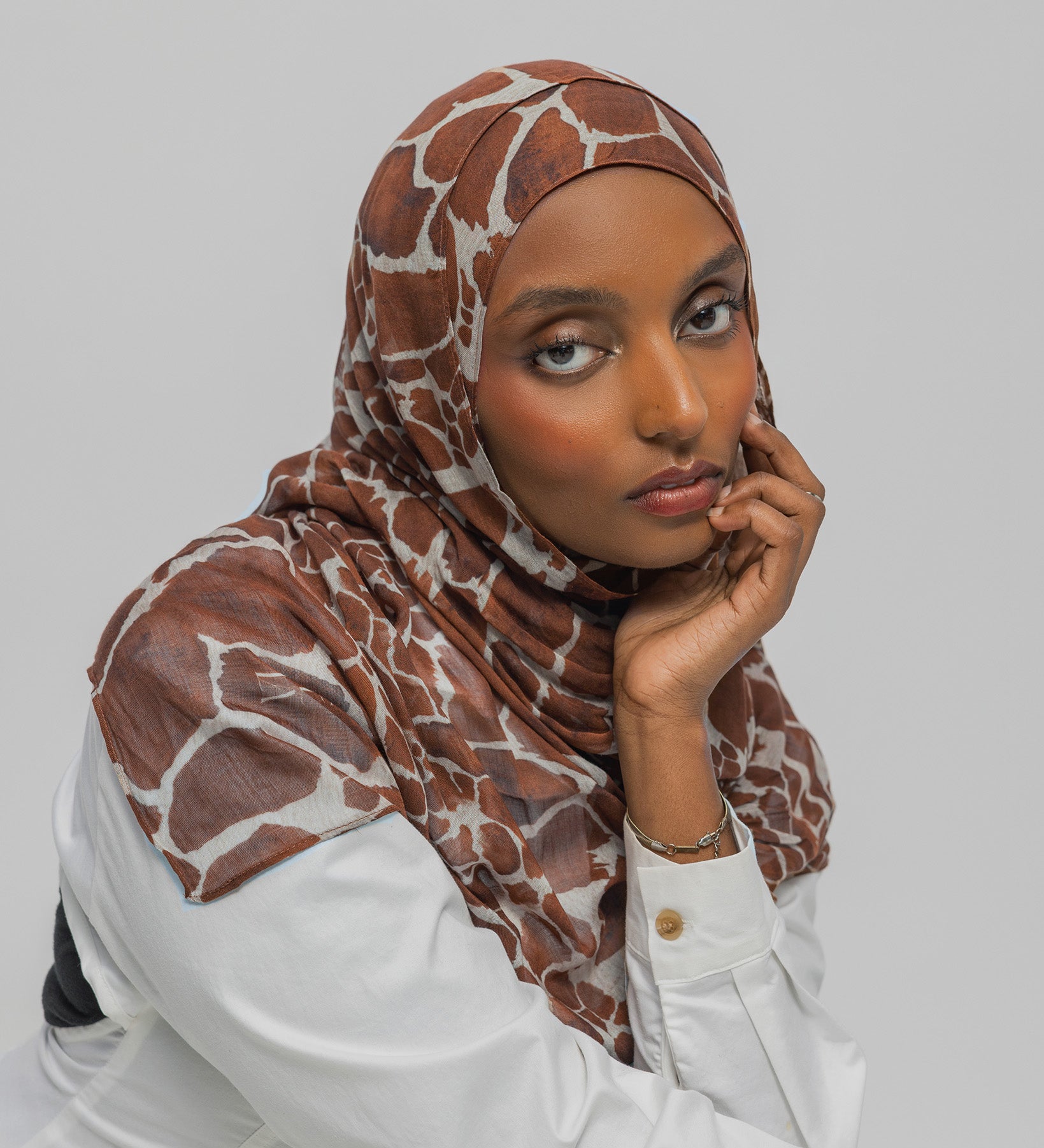 Woman wearing a giraffe patterned hijab and white shirt against a plain background
