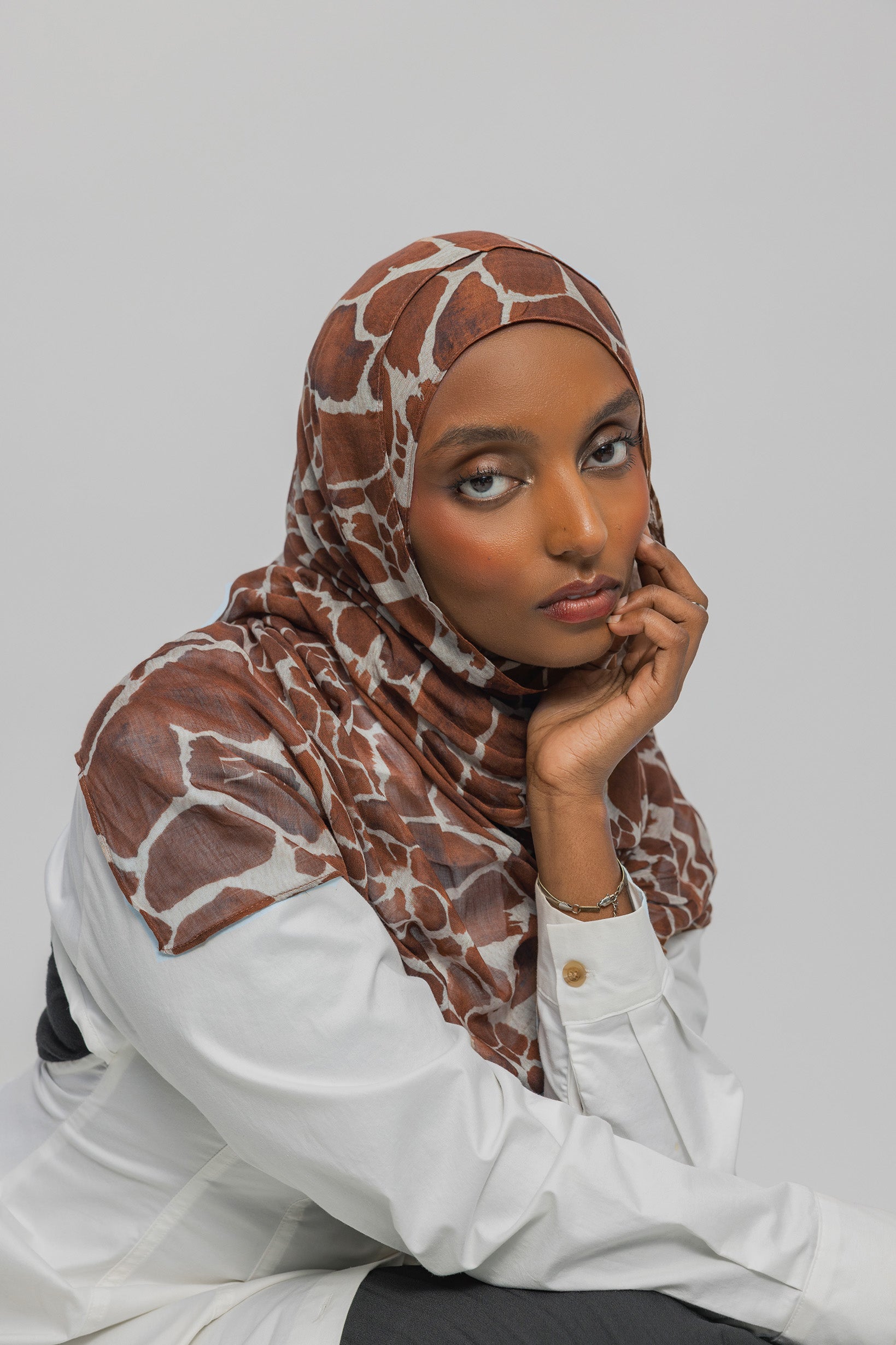 Woman wearing a giraffe patterned hijab and white shirt against a plain background