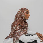 Woman wearing a patterned hijab against a plain background