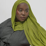 Woman wearing a green hijab and gray outfit against a white background
