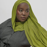 Woman wearing a green hijab and gray outfit against a white background