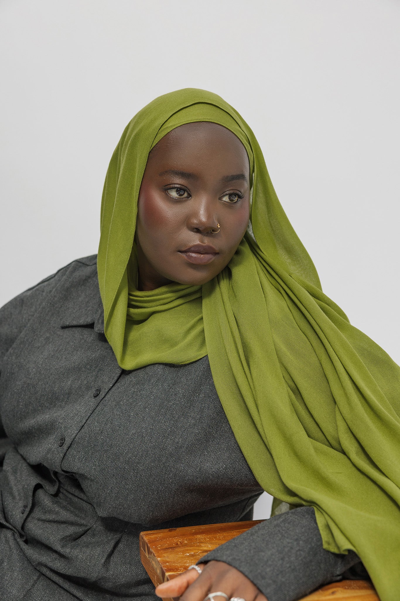 Woman wearing a green hijab and gray outfit against a white background