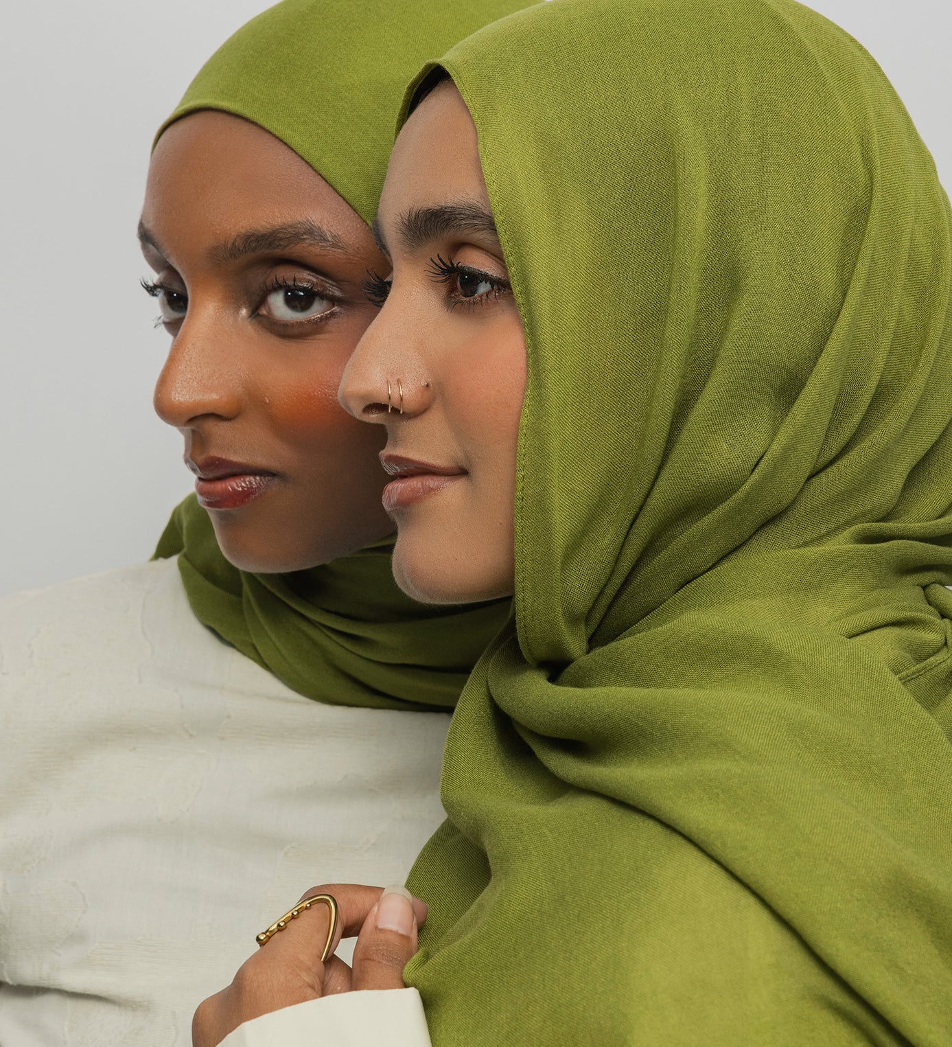 Two women wearing green hijabs and white clothing against a plain background