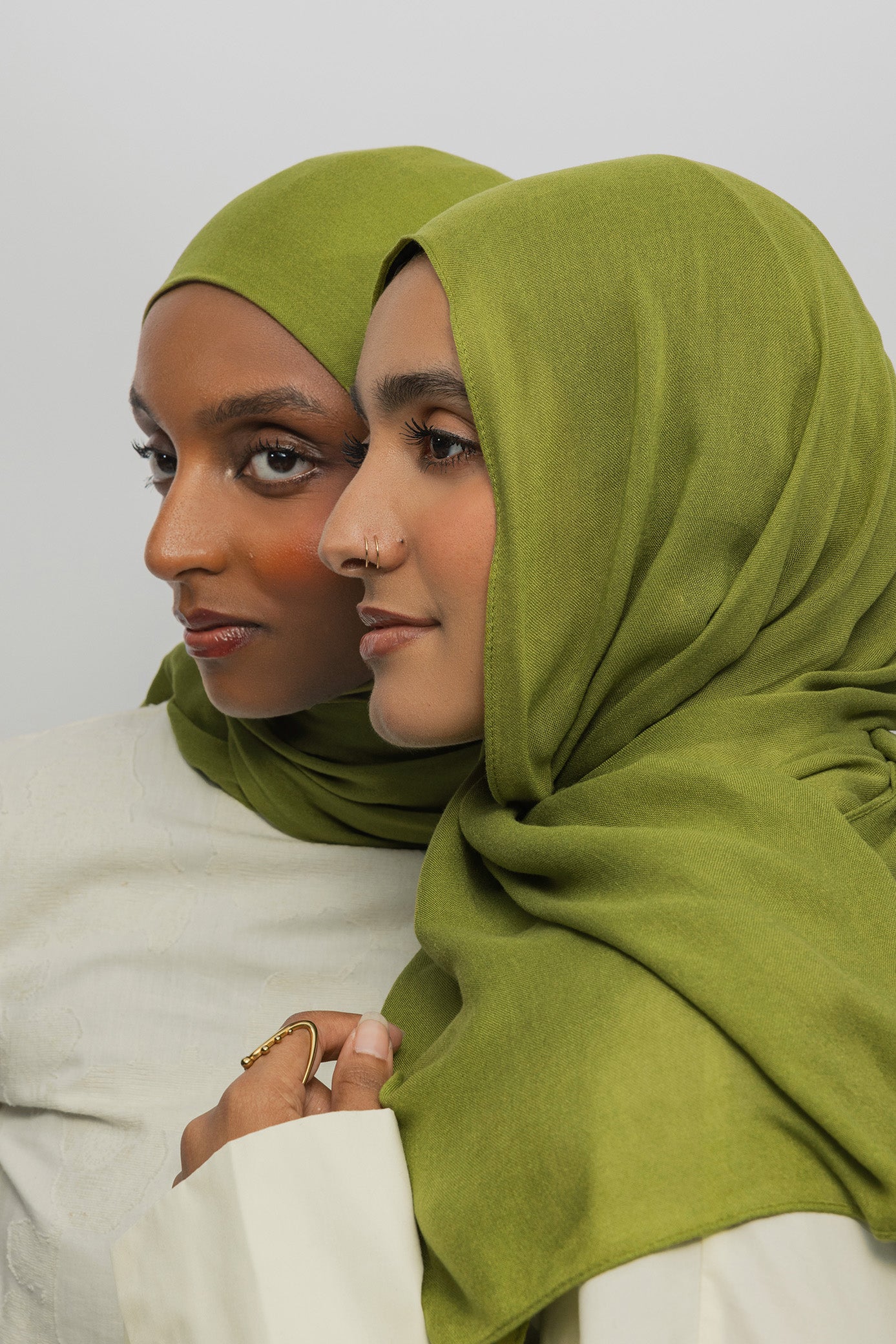 Two women wearing green hijabs and white clothing against a plain background