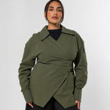 A woman modeling an olive green wrap-style long-sleeve shirt with a belted waist, worn over a black top and black wide-leg pants, against a light gray studio background.