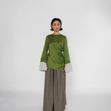 Woman wearing a green top with striped cuffs and brown wide-leg pants on a white background