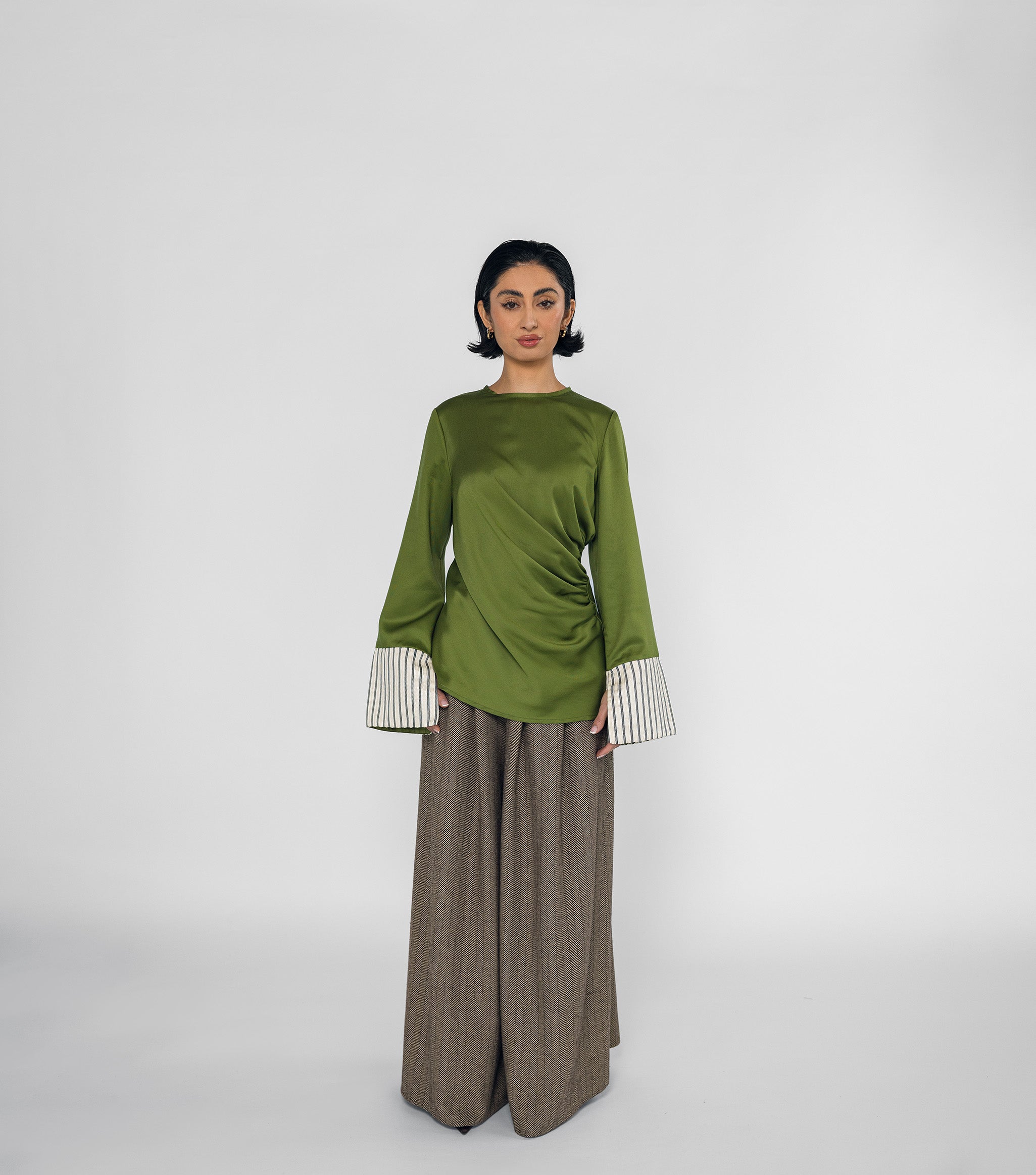 Woman wearing a green top with striped cuffs and brown wide-leg pants on a white background