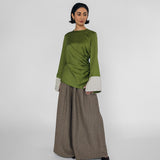 Woman wearing a green top with white cuffs and a brown pants on a white background