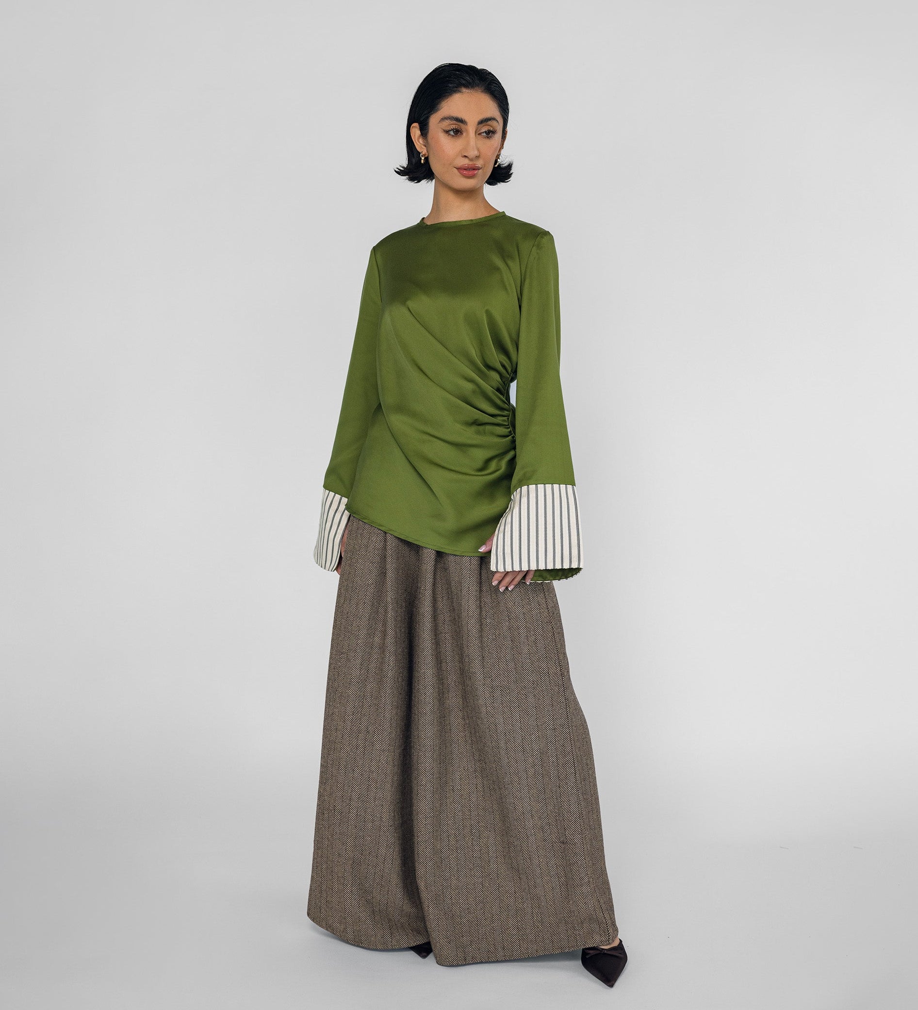 Woman wearing a green top with white cuffs and a brown pants on a white background