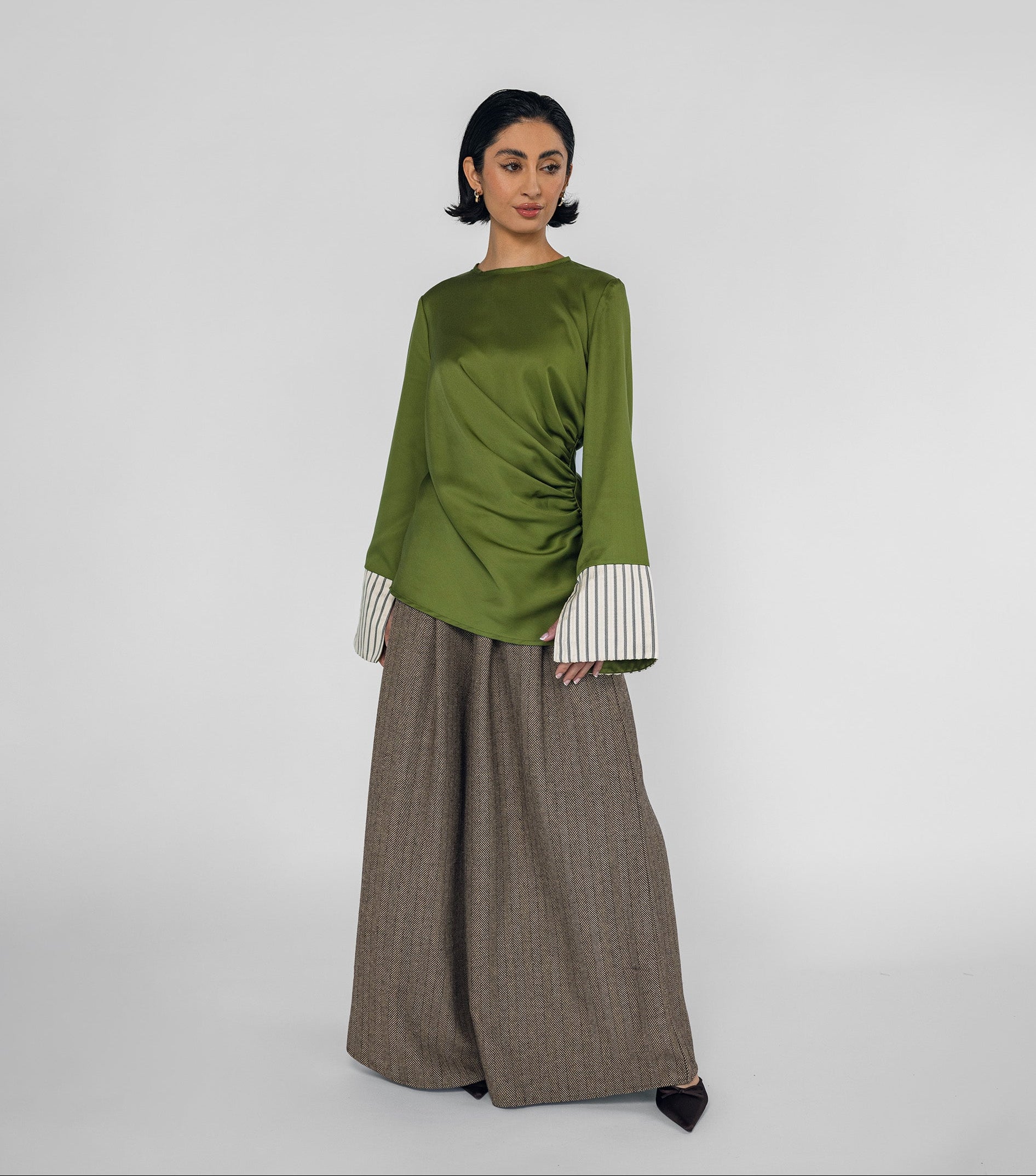 Woman wearing a green top with white cuffs and a brown pants on a white background