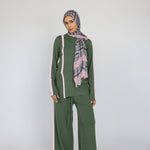 Woman wearing a green matching outfit with a pink plaid lace scarf on a white background