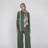 Woman wearing a green matching outfit with a pink plaid lace scarf on a white background