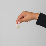 Hand holding a gold Henna charm against a gray background