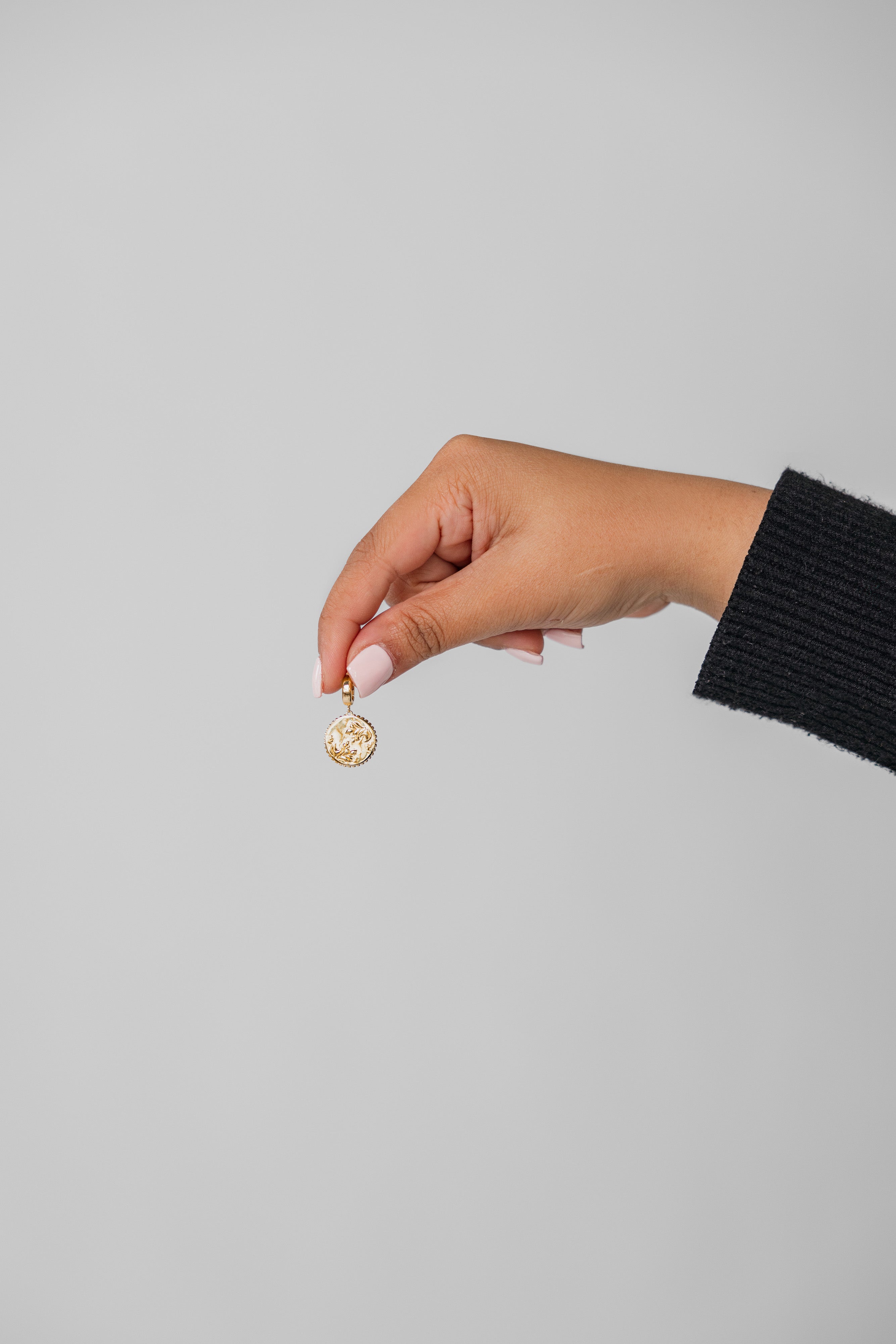 Hand holding a gold Henna charm against a gray background