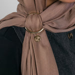 Close-up of a brown hijab with a gold ring and Henna Charm worn by a person.