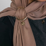 Close-up of a brown hijab with a gold ring and Henna Charm worn by a person.