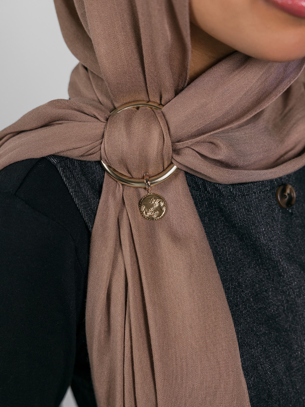Close-up of a brown hijab with a gold ring and Henna Charm worn by a person.