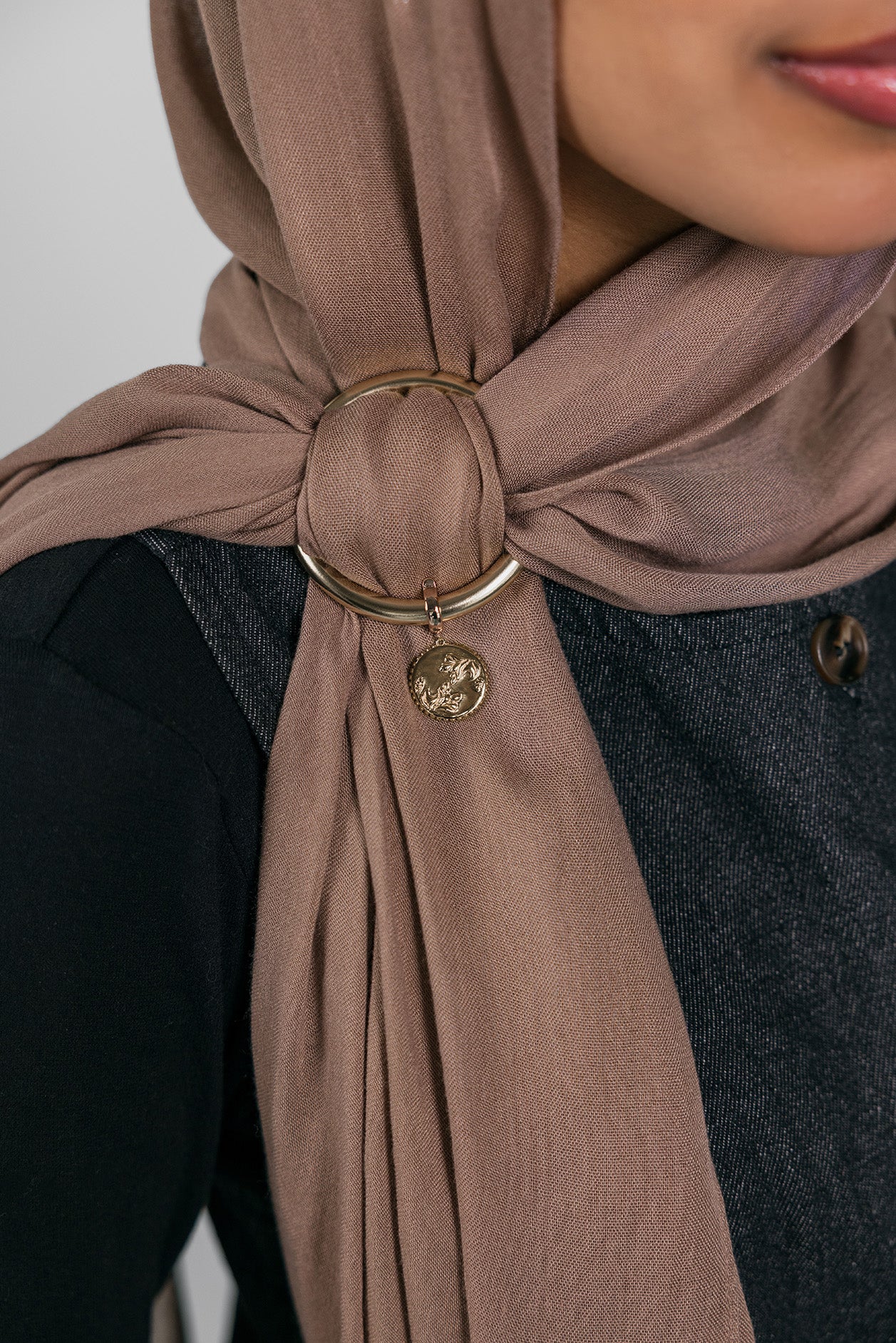 Close-up of a brown hijab with a gold ring and Henna Charm worn by a person.