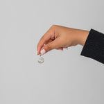 Hand holding a silver Henna Charm against a plain background