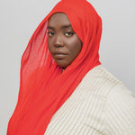 Person wearing a red hijab and beige top against a gray background
