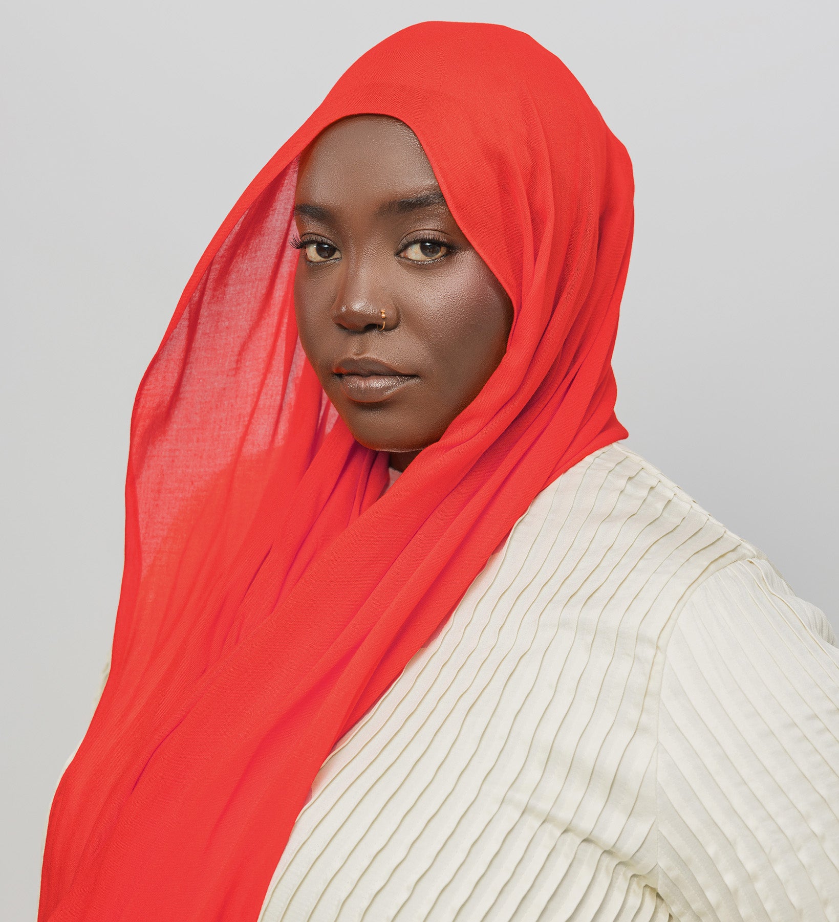 Person wearing a red hijab and beige top against a gray background