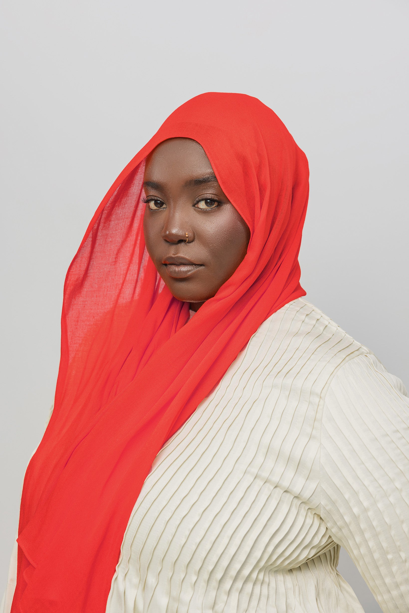 Person wearing a red hijab and beige top against a gray background