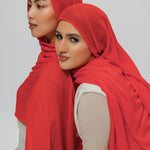 Two women wearing red hijabs against a plain background