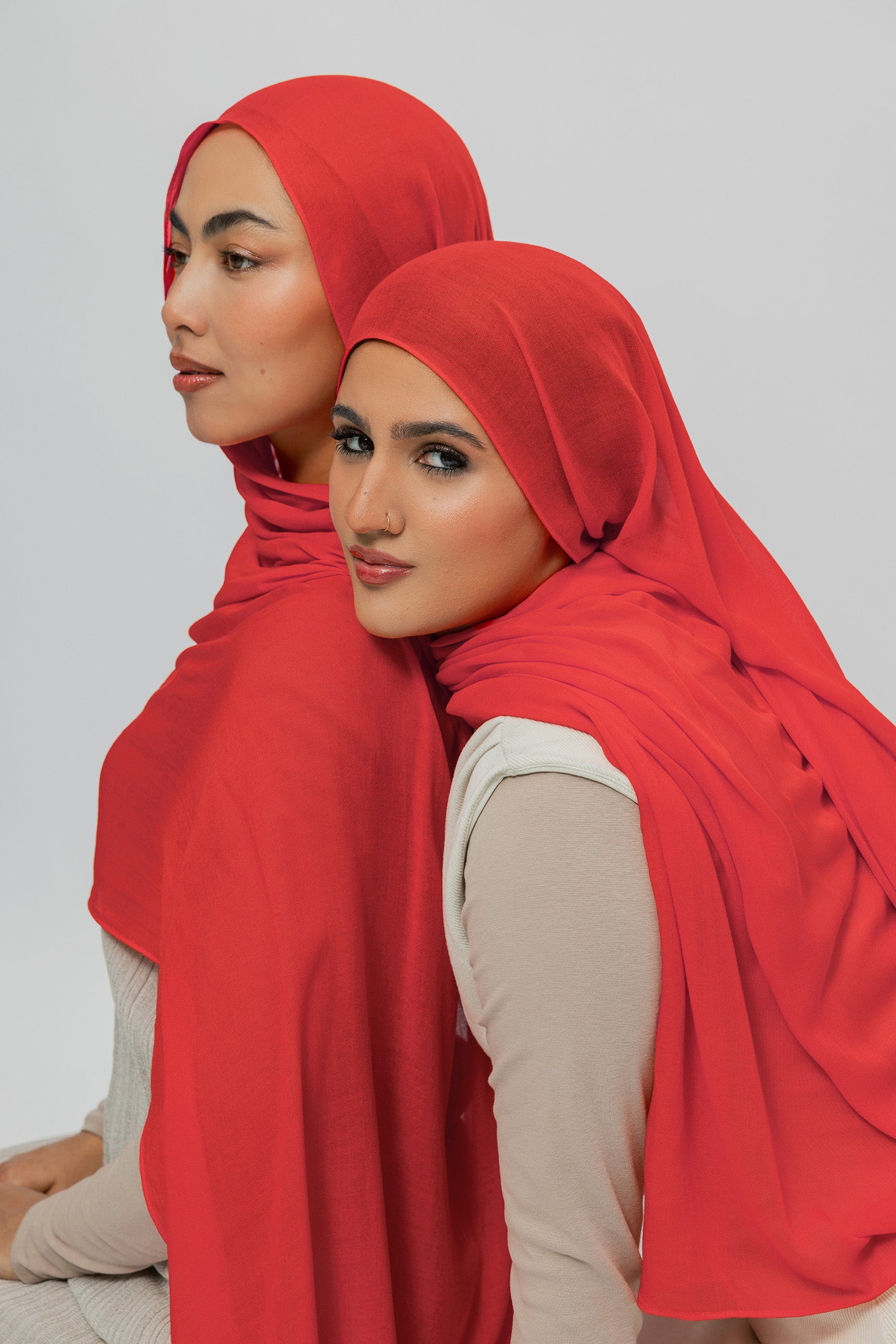 Two women wearing red hijabs against a plain background