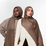 Two models wearing brown patterned hijabs and shawls with gold stripes, styled with neutral-colored tops against a plain white studio background.