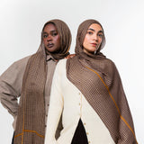 Two models wearing brown patterned hijabs and shawls with gold stripes, styled with neutral-colored tops against a plain white studio background.