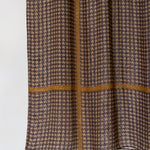A close-up of a brown and beige houndstooth patterned fabric with a contrasting tan cross-stitch design, shown against a plain white background.