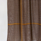A close-up of a brown and beige houndstooth patterned fabric with a contrasting tan cross-stitch design, shown against a plain white background.