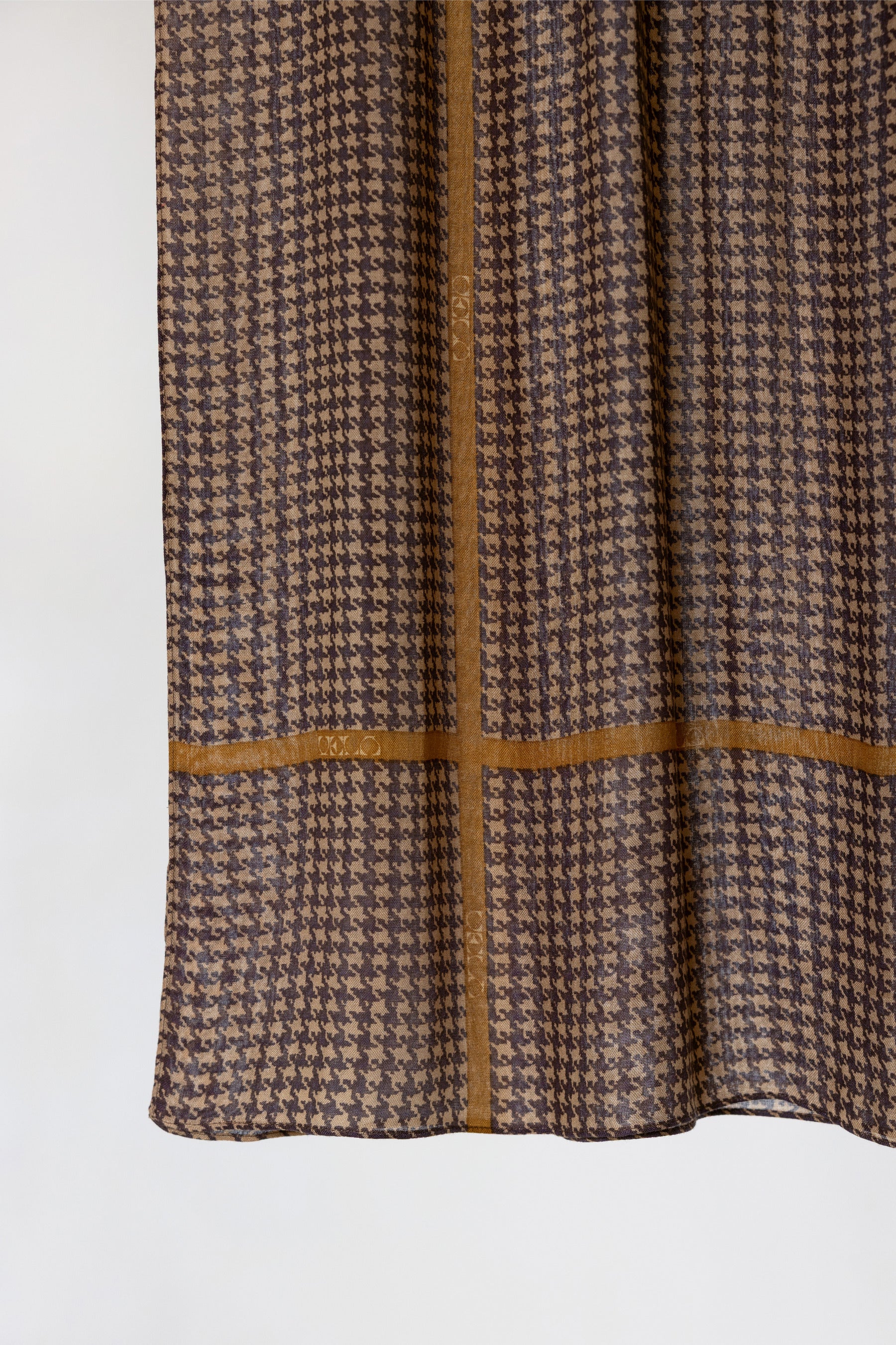A close-up of a brown and beige houndstooth patterned fabric with a contrasting tan cross-stitch design, shown against a plain white background.
