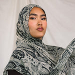 Close up shot of model wearing the Ink Cobra scarf by VELA, featuring a cool-toned, grey scale, snakeskin pattern on the scarf. 