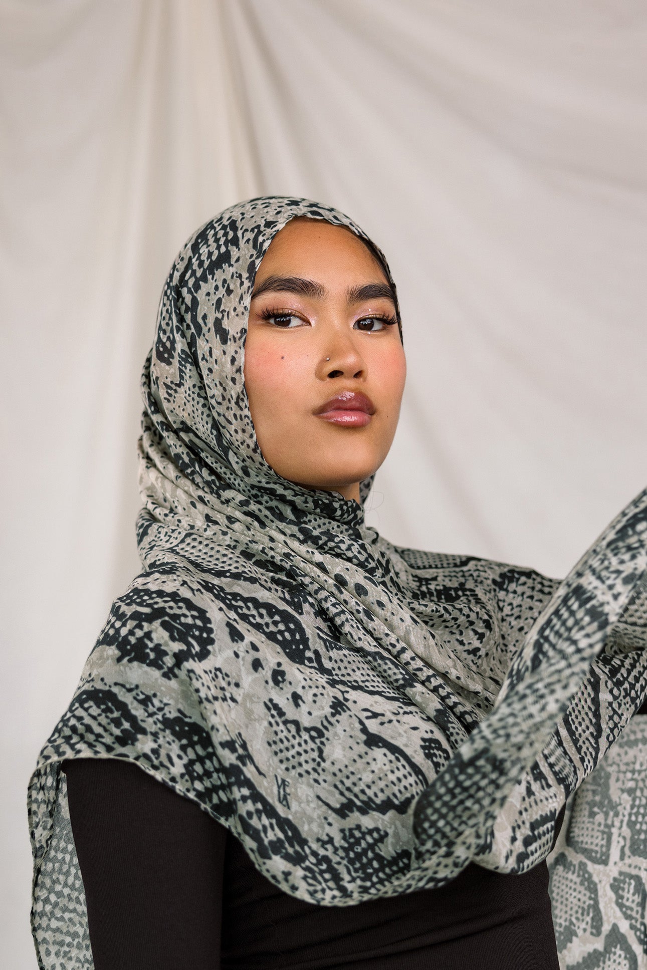 Close up shot of model wearing the Ink Cobra scarf by VELA, featuring a cool-toned, grey scale, snakeskin pattern on the scarf. 