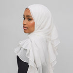A woman wearing a white ruffled hijab, shown in profile against a plain light gray studio background.