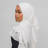 A woman wearing a white ruffled hijab, shown in profile against a plain light gray studio background.