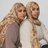 Two women wearing ivory patterned hijabs against a plain background