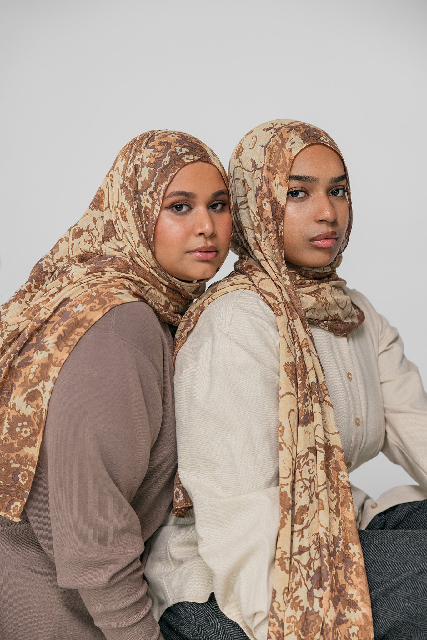 Two women wearing ivory patterned hijabs against a plain background
