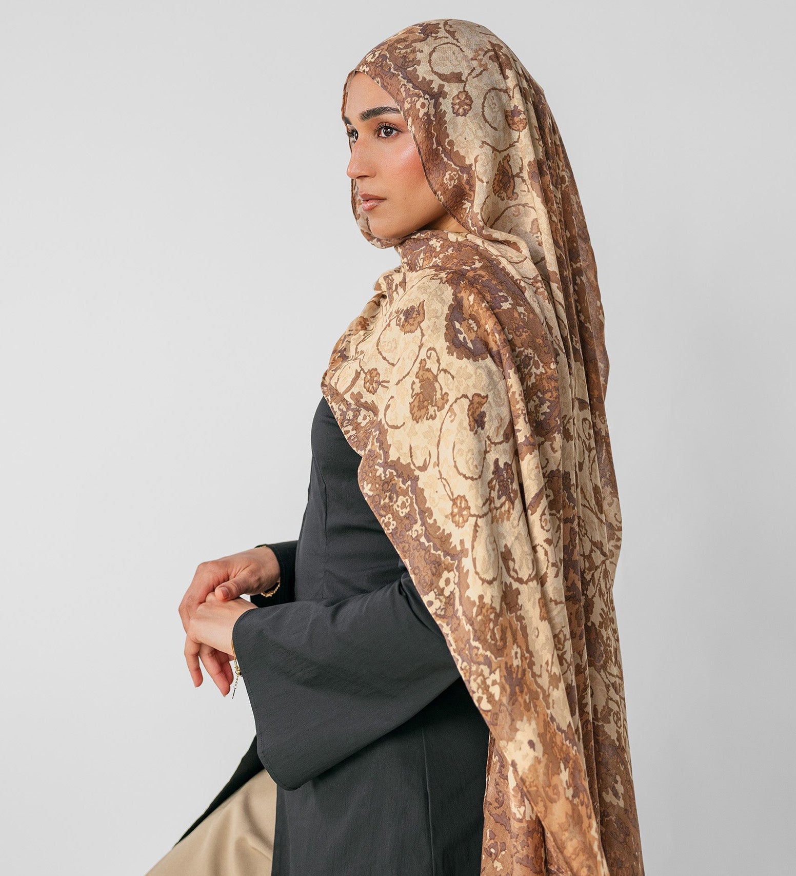 Woman wearing a ivory patterned hijab on a plain background