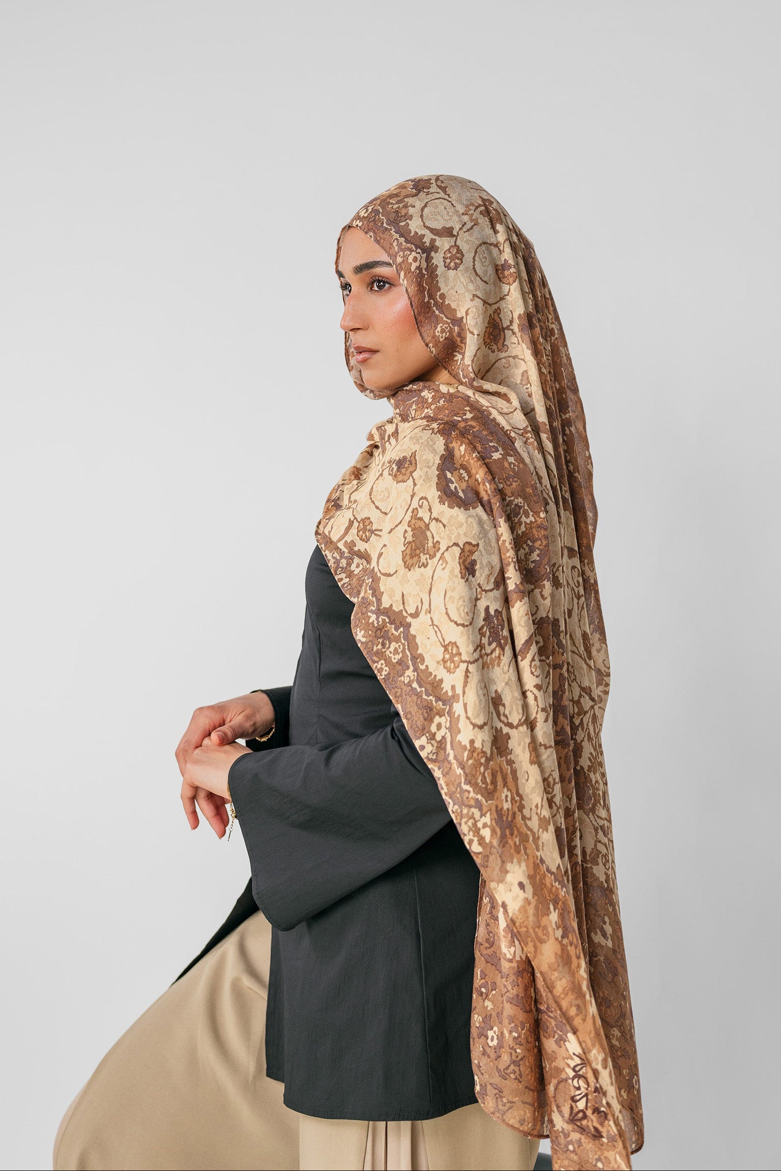 Woman wearing a ivory patterned hijab on a plain background