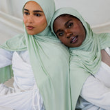  Two models side by side wearing Sage Mist Jersey Lite, showcasing its fresh minty-green tone in both natural and styled wraps.