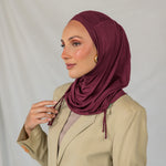 Woman wearing a burgundy ruched hijab and beige blazer against a plain background.